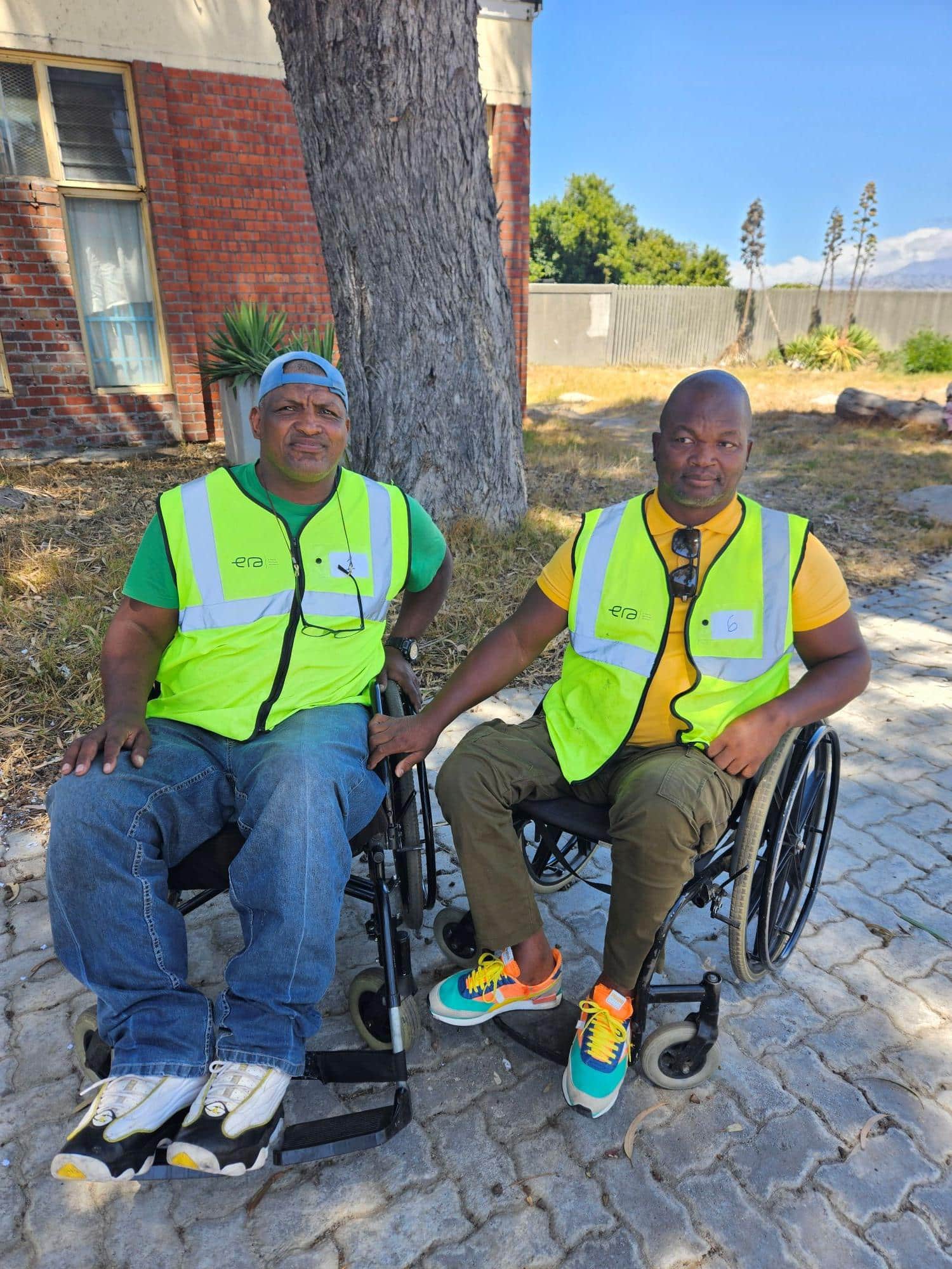 Two wheelchair bound men smile proudly in their ERA NPC and N.E.E.D vests.